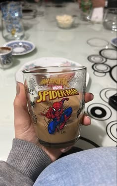 a person holding up a glass with spiderman on it in front of a table