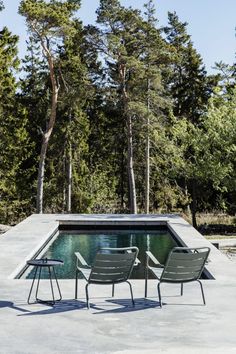 two lawn chairs sitting next to a pool in the middle of a forest with trees