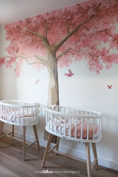 two white cribs with pink trees painted on the wall