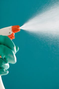 a person in green gloves spraying water with a white sprayer on a blue background