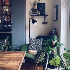 a living room filled with lots of plants next to a wooden table and chair in front of a window