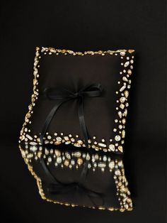 a black square pillow with gold and white beads on the edges, tied with a black ribbon