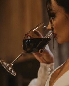 a woman holding a glass of red wine up to her face and looking at it