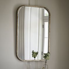 a mirror hanging on the wall above a table with vases and flowers in it