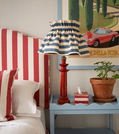 a blue table with a lamp on it next to a red and white striped headboard