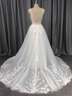 a white wedding dress on display in front of a gray curtain and grey curtains behind it