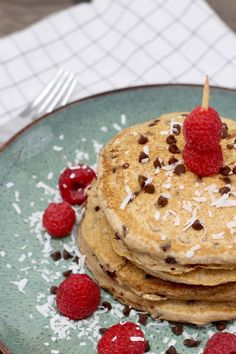 a stack of pancakes topped with raspberries and chocolate chips on a blue plate