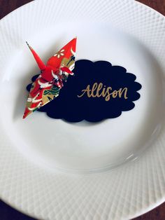 a white plate topped with an origami bird on top of it's name