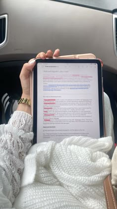 a woman is holding an electronic device in her hand while sitting in the back seat of a car