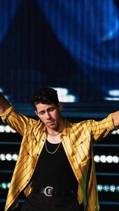 a male in a yellow shirt is holding his hands up to the side while standing on stage