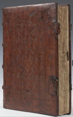 an old leather book with intricate carvings on the front and sides, opened to show pages