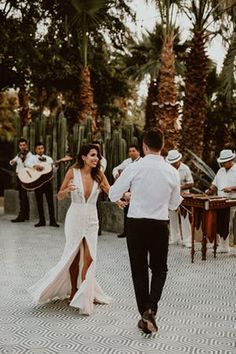 a man and woman dancing in front of some people playing instruments on the street with cactus trees behind them