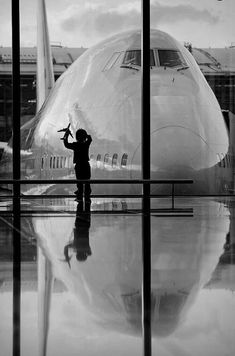 a black and white photo of an airplane at the airport with its reflection on the ground