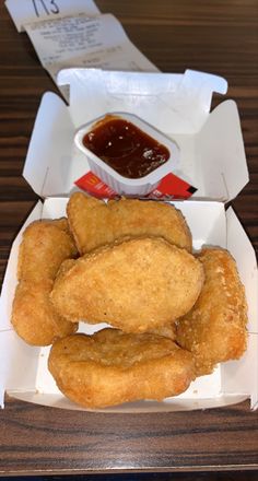 some fried food is in a box on a table with ketchup and sauce