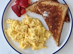 scrambled eggs, toast and strawberries are on a white plate with blue rims