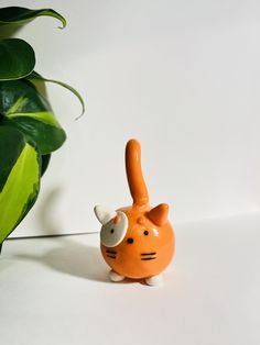 an orange cat figurine next to a potted plant on a white surface