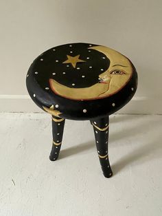 a small black stool with a yellow moon and star painted on the top, sitting against a white wall