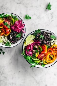 two bowls filled with colorful vegetables and rice on top of a marble countertop next to lime wedges