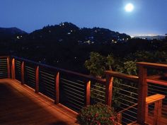 a full moon is seen over the city lights from a deck at night with wooden railings and planters