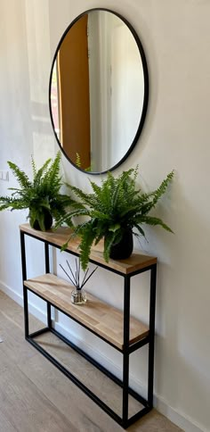 a mirror on the wall next to a wooden shelf with two plants and a bench