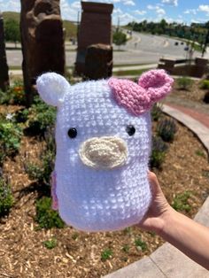 a hand holding up a crocheted stuffed animal with a pink bow on it's head