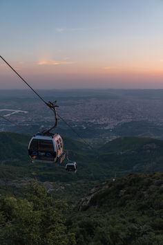 a cable car going up the side of a mountain with trees on both sides at sunset