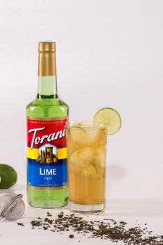 a bottle of torani lime next to a glass filled with lemonade and garnish