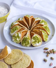 a plate filled with crackers covered in green and white toppings next to other snacks