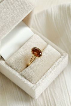 a gold ring with an orange stone sits in a white box