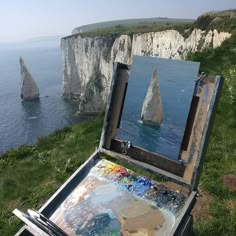 an artist's easel sitting on top of a grass covered hill next to the ocean