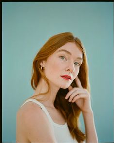 a woman with long red hair is posing for a photo in front of a blue background