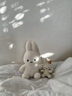 two stuffed animals sitting on top of a bed next to each other in the sunlight