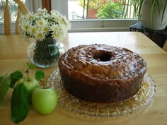 a cake sitting on top of a glass plate next to an apple and flower vase