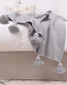 a white bed topped with a gray blanket and two pom poms