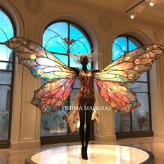 a woman is standing in front of two large windows with stained glass wings on them