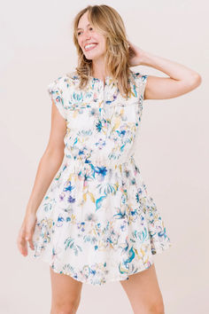 a woman wearing a white dress with blue and yellow flowers on it, posing for the camera