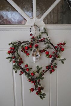 a heart shaped wreath hanging on the front door with bells and holly berries attached to it