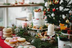 a table topped with lots of different types of cakes and desserts next to a christmas tree