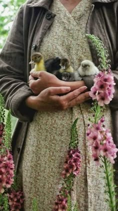 a woman is holding three small birds in her hands while surrounded by flowers and plants