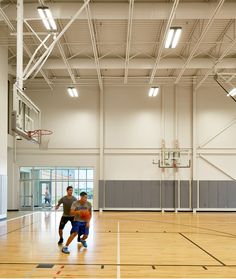 two men are playing basketball in an indoor gym with hard wood floors and white walls