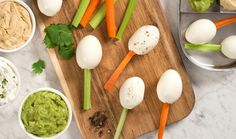 an assortment of vegetables on a cutting board with dips and guacamole