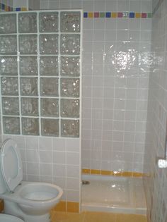 a white toilet sitting in a bathroom next to a bathtub and tiled walls with glass blocks on it