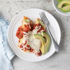 a white plate topped with lasagna covered in sauce and cheese next to an avocado