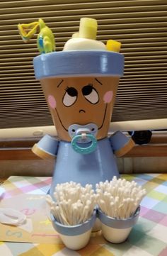 a baby doll sitting on top of a table next to two cups filled with toothbrushes