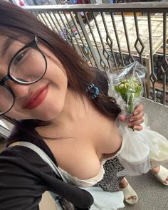 a woman with glasses holding flowers and looking at the camera while standing next to a railing