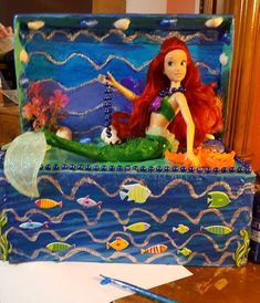 a little mermaid doll sitting on top of a blue box