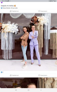 two women standing next to each other in front of a wall with flowers and decorations