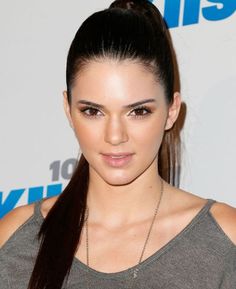 a woman with long hair wearing a gray shirt and black leather skirt posing for the camera