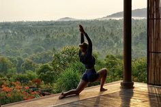 a woman is doing yoga on a porch overlooking the trees and mountains in front of her