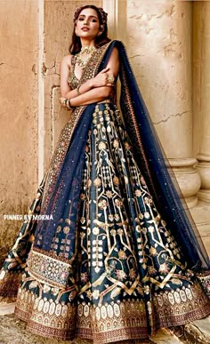 a woman in a blue and gold bridal gown leaning against a wall with her arms crossed